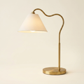 Ornate Brass Ring Base Curved Table Lamp With Triangle White Drum Shad on a warm cream background